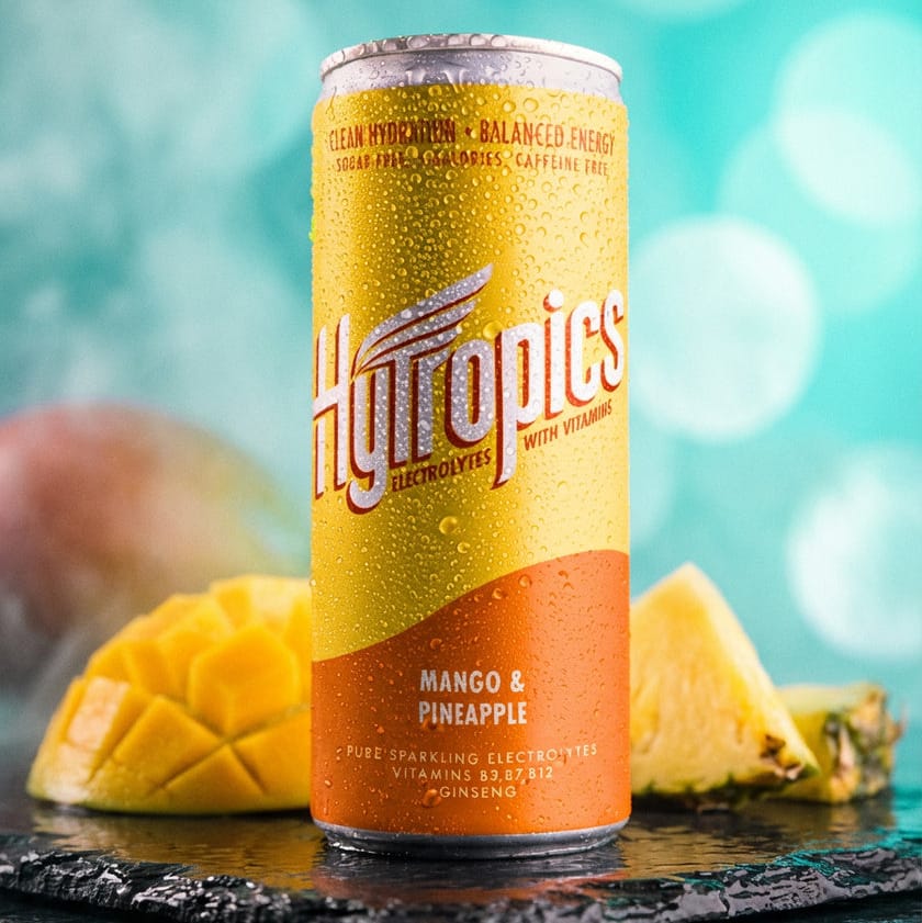 Hytropics Mango & Pineapple energy drink can with mango and pineapple on a blurred background