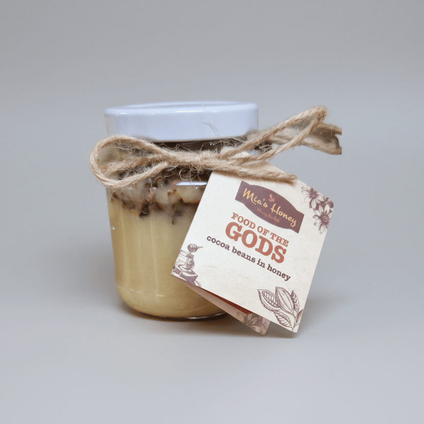 Jar of 'Food of the Gods' cocoa beans in honey with a decorative bow and tag on a white background