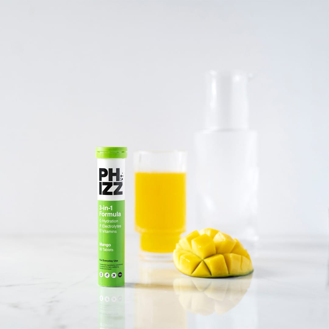 PHIZZ supplement bottle with a glass of orange juice and a mango on a white background