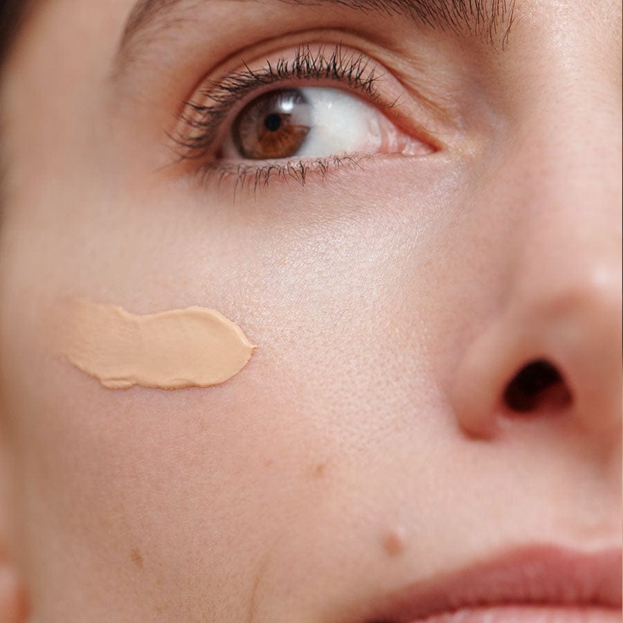 Close-up of a person's face with a smear of beige liquid foundation on the cheek.