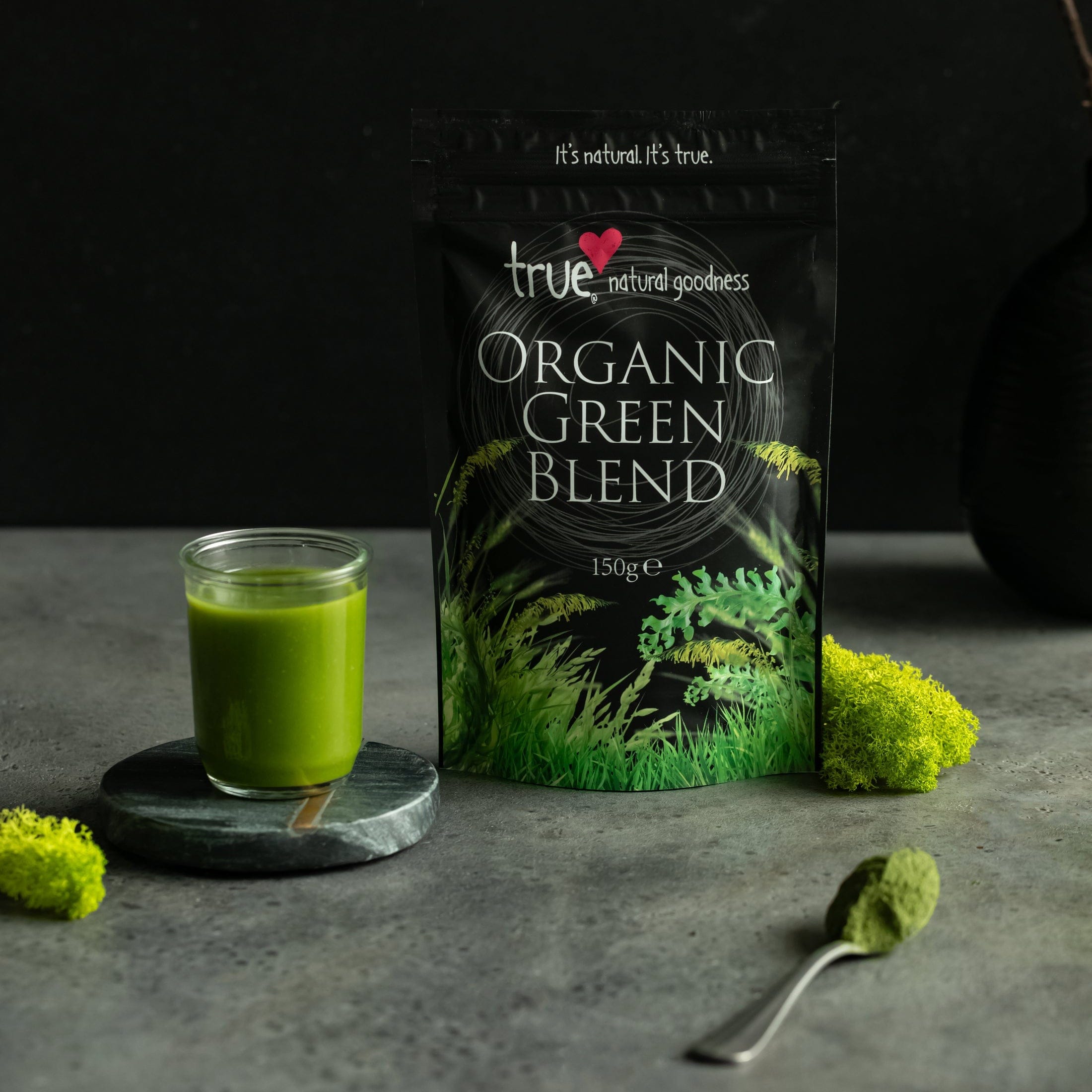 Bag of true organic green blend with a glass of green juice on a dark background