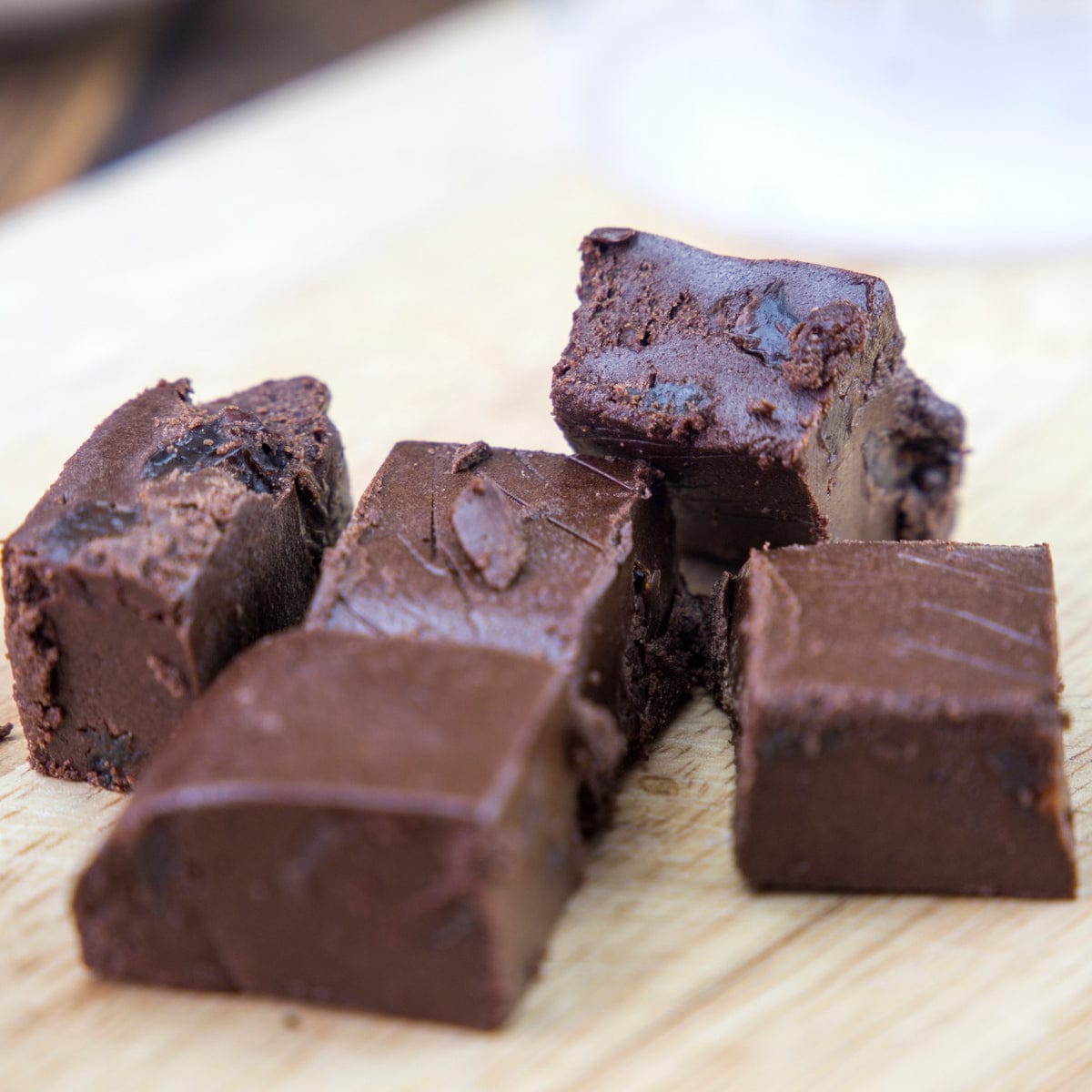 Several pieces of dark chocolate fudge or brownie with visible cookie-dough chunks, arranged on a light wood surface.