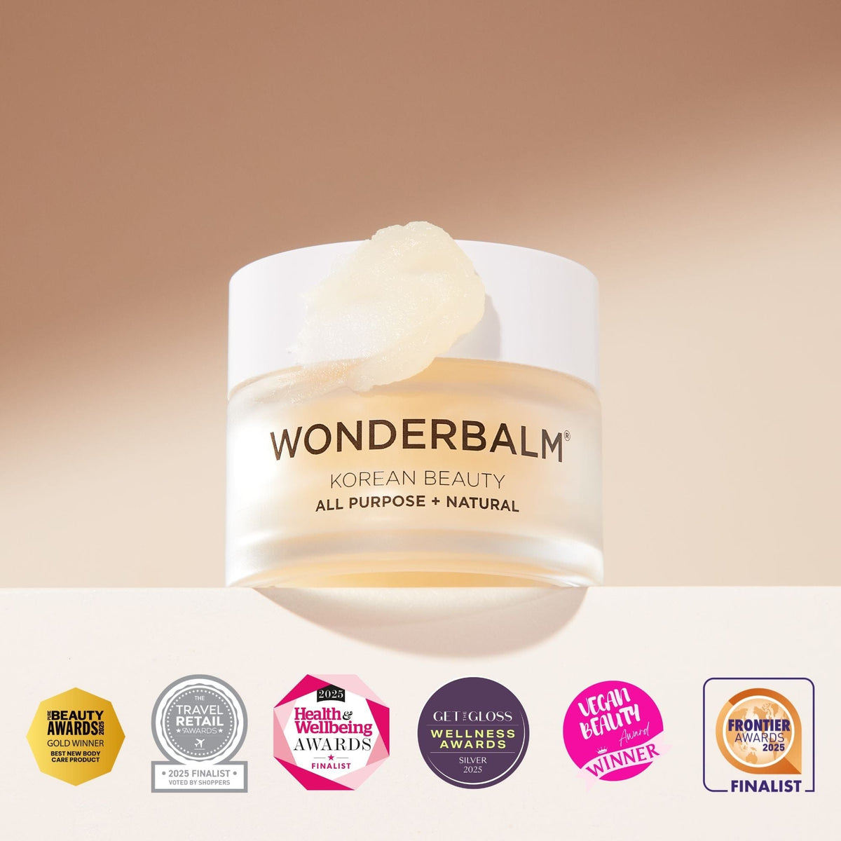 Wonderbalm Korean Beauty All Purpose + Natural cream jar with a white lid and a dollop of cream on top, shown against a warm beige gradient background with several award badges along the bottom.